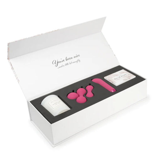 Coffret ouvert avec bougie en pot, trois accessoires roses, appareil rose et cartes rangés dans la mousse